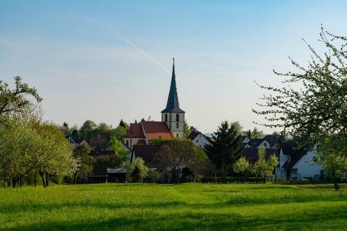 Grüne saftige Wiese im Vordergrund. Im Hintergrund ist der Kirchturm von Amrichshausen zu sehen.